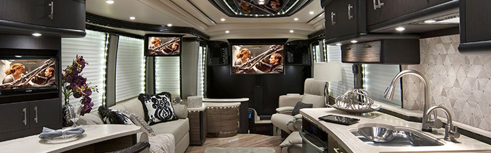 Interior of an RV with multiple television screens and surround sound (background)